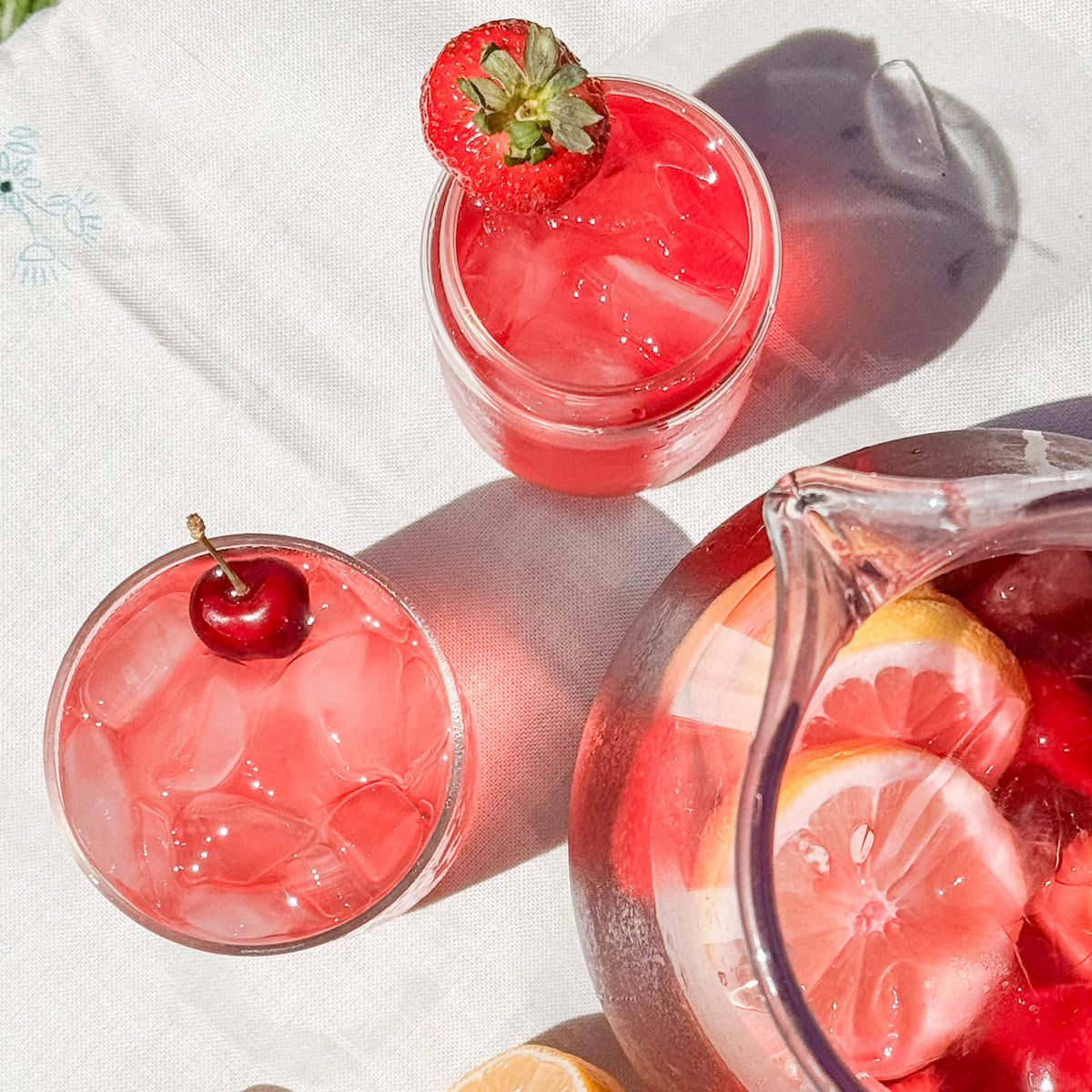 Pink lemonade with strawberries and cherries on a white surface