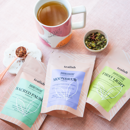 Tea bags labeled 'Sacred Pause', 'Moonbrew', and 'First Light' with a mug of tea on a pink surface.