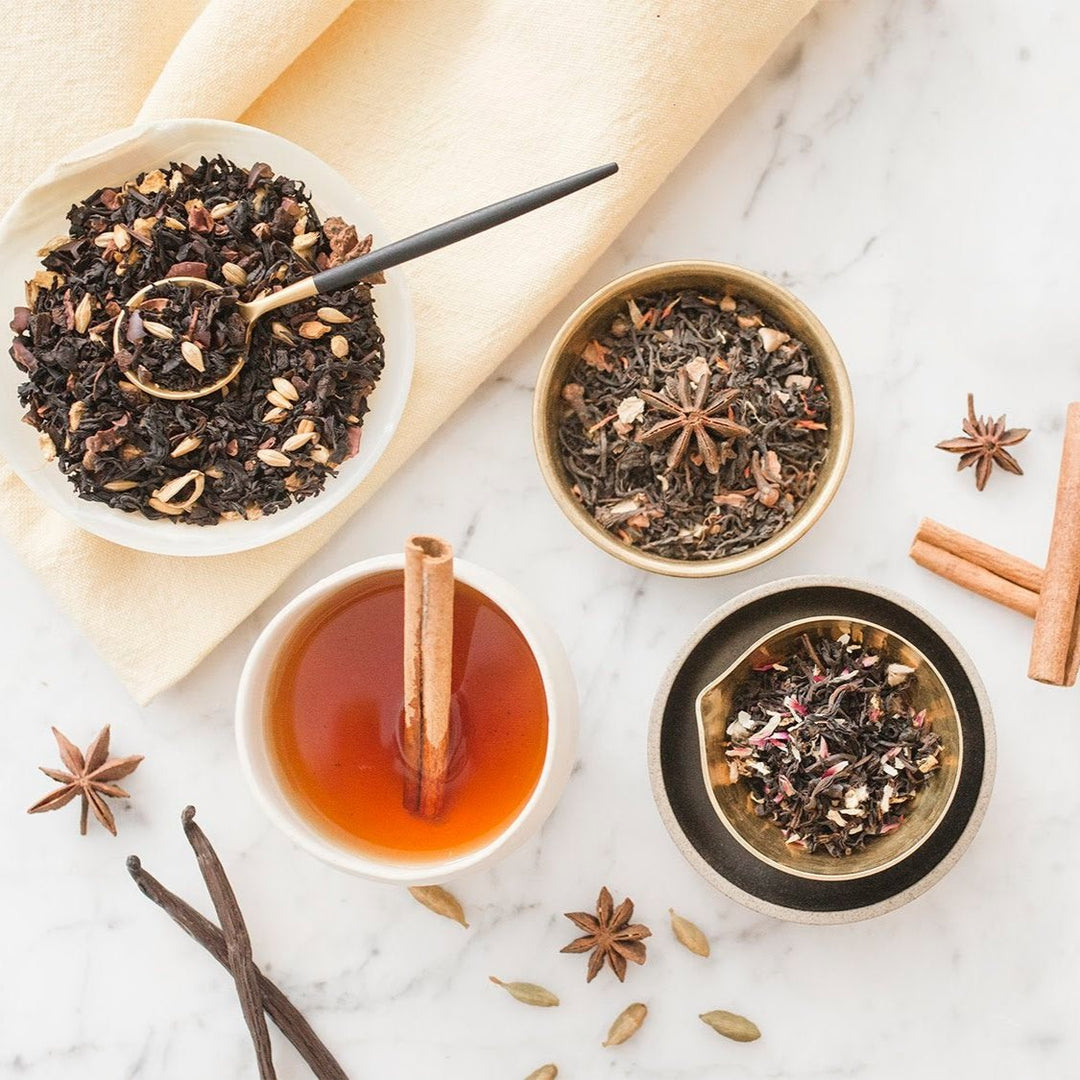 An overhead shot of various tea blends, with a prominent black tea mix labeled as 'Chai Darling', accompanied by spices like cinnamon and anise stars, and a cup of brewed tea.