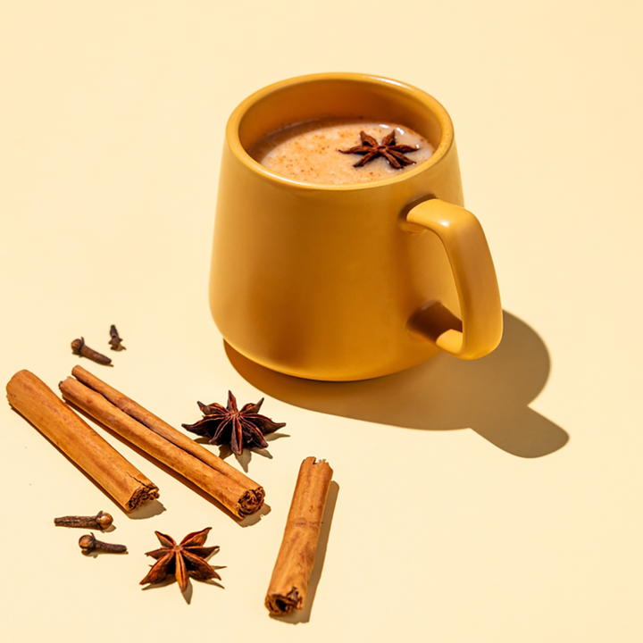 A cup of Chai Rooibos tea with spices such as cinnamon sticks and star anise displayed alongside.