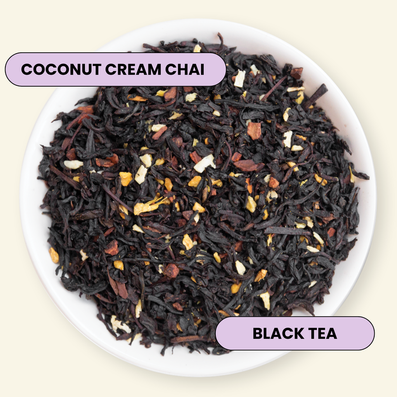 A top-down view of loose-leaf black tea in a white bowl, labeled 'COCONUT CREAM CHAI' and 'BLACK TEA' on light purple text badges. The tea blend is predominantly very dark brown to black with visible coconut flakes and small dried fruit pieces.
