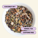 A top-down view of a white bowl filled with loose herbal tea blend labeled 'COCONUT SKY', with text callouts reading 'COCONUT SKY', 'HERBAL TEA', and 'CAFFEINE FREE' on a pale cream background.
