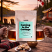 Tea packaging with 'Coming to the Cottage' text, two mugs of tea, and a scenic background with a lake and cabin.