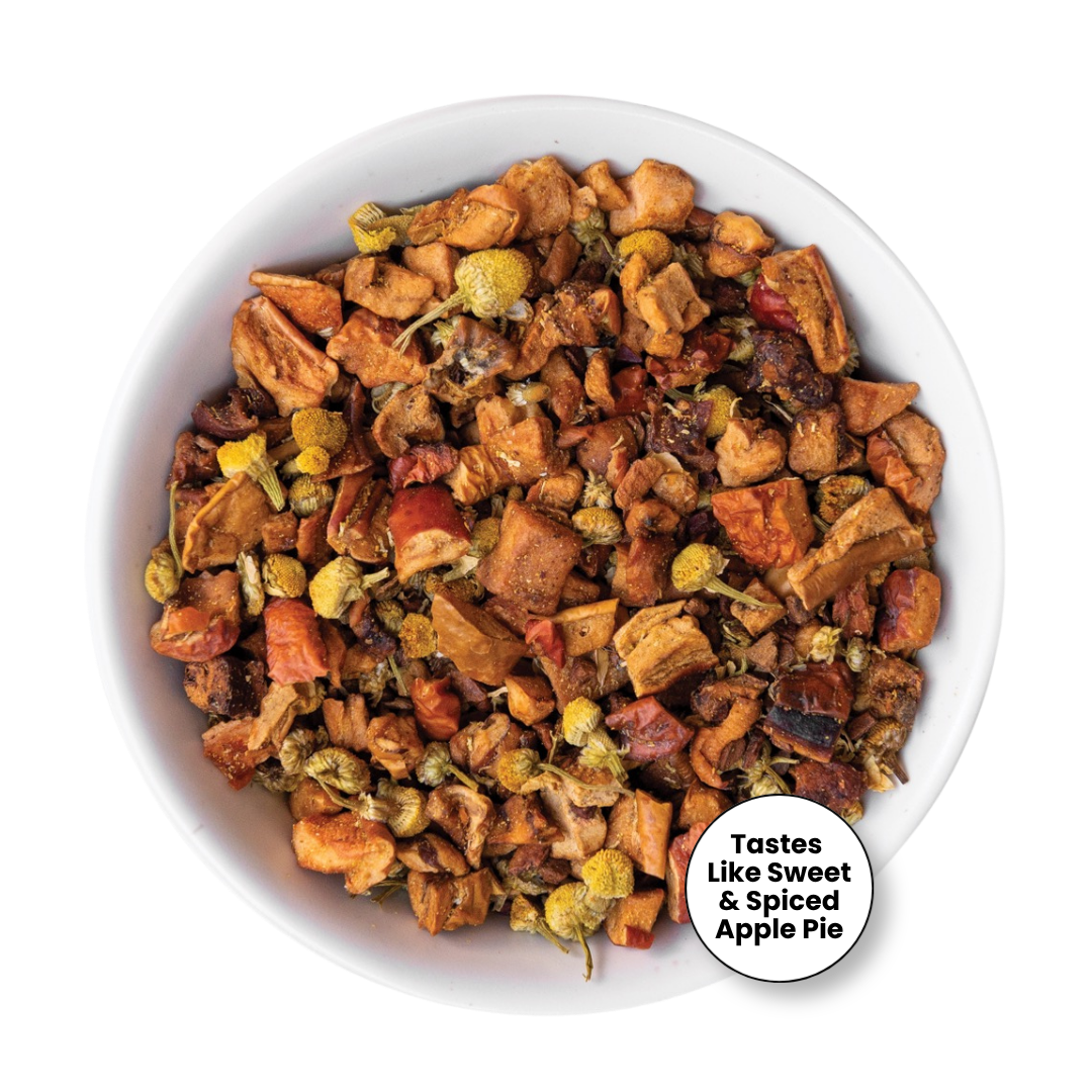 A top-down view of a white bowl filled with a loose-leaf herbal tea blend. The tea contains pieces of dried apple, orange peel, and small yellow flower buds.