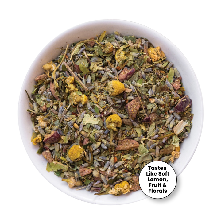 A top-down view of a white bowl filled with loose herbal tea blend, featuring dried flowers, leaves, and botanical pieces. A white circular badge in the lower right corner reads, &
