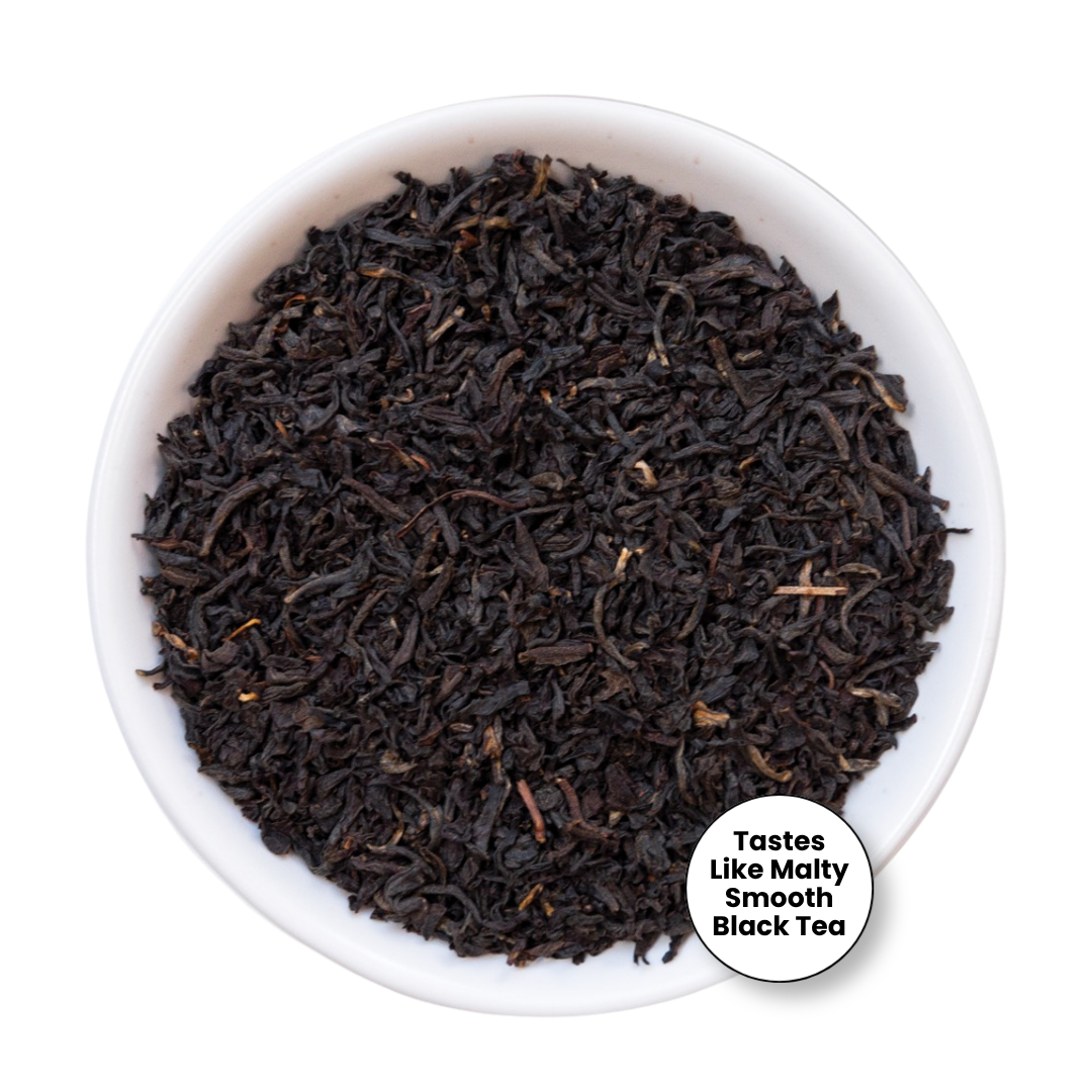 A top-down view of loose-leaf black tea filling a white ceramic bowl, with a small white circular label in the lower right that reads &