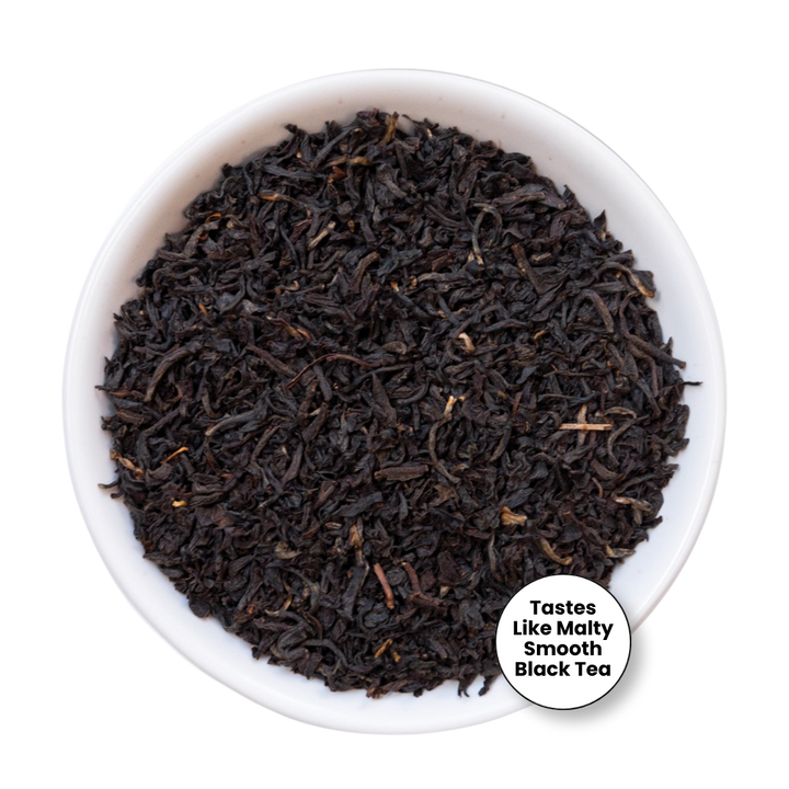 A top-down view of loose-leaf black tea filling a white ceramic bowl, with a small white circular label in the lower right that reads &