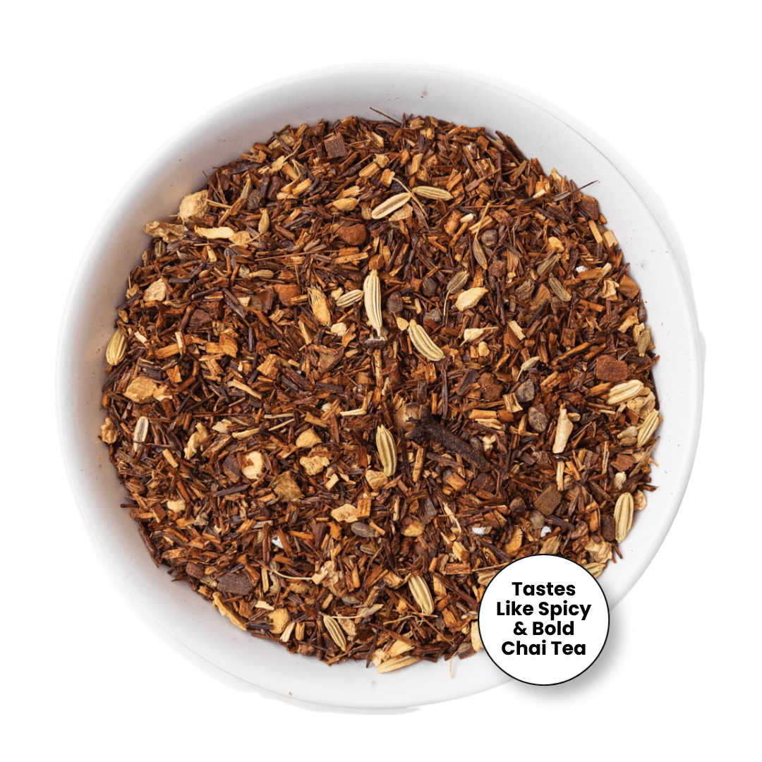 A top-down view of loose-leaf herbal tea blend in a white bowl, featuring dark brown and reddish-brown pieces with beige seeds and botanicals. A white circular badge in the lower right reads &