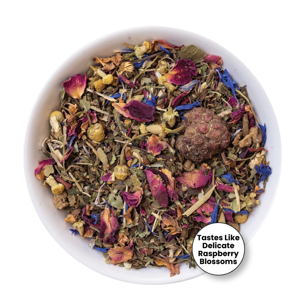 A white bowl filled with loose-leaf herbal tea blend featuring dried flowers, petals, herbs, and a round brown tea ball, with a white circular badge in the lower right reading 'Tastes Like Delicate Raspberry Blossoms'.