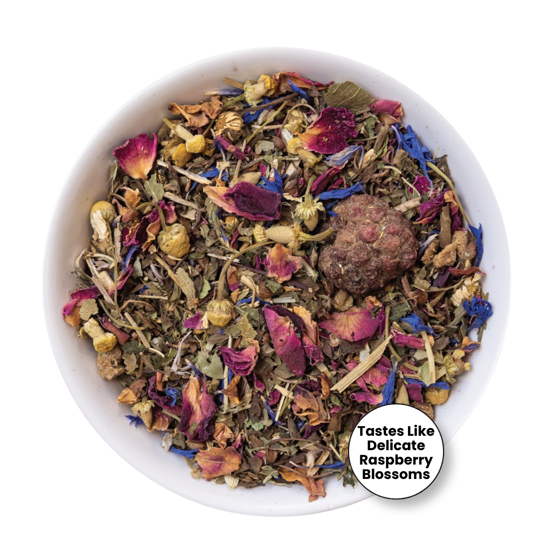 A white bowl filled with loose-leaf herbal tea blend featuring dried flowers, petals, herbs, and a round brown tea ball, with a white circular badge in the lower right reading &