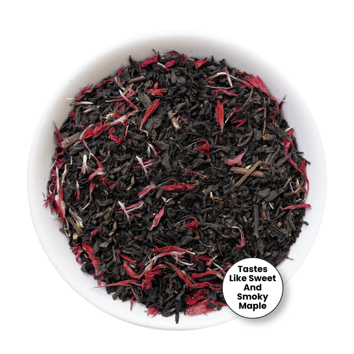 A top-down view of loose-leaf tea inside a white bowl, featuring dark black tea leaves mixed with bright red dried flower petals. A circular badge in the bottom right corner reads &