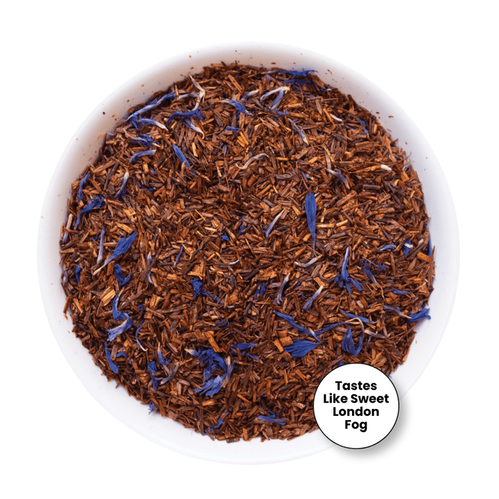 A top-down view of loose-leaf tea in a white bowl, featuring brown tea leaves mixed with blue flower petals. A small white circular badge in the bottom right corner reads &