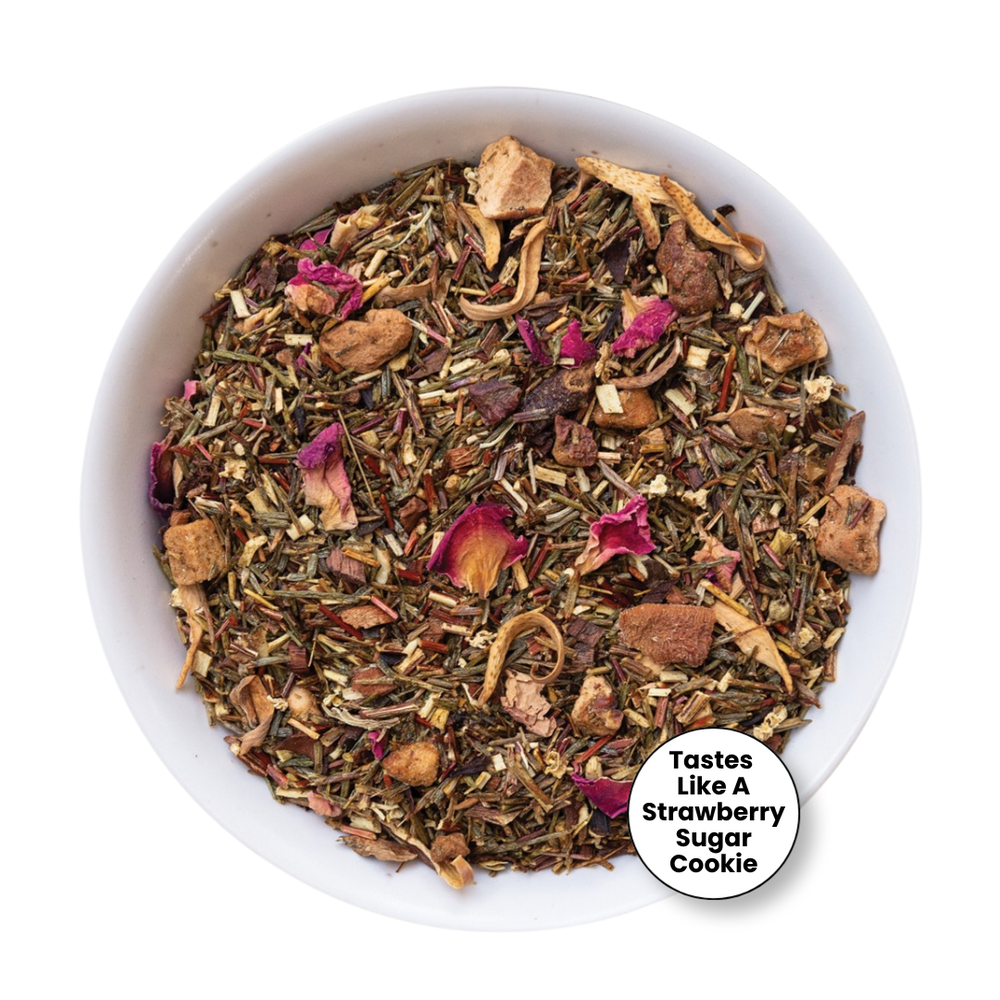A top-down view of a white bowl filled with a loose-leaf herbal tea blend. The tea contains dried green herbs, brown pieces, and pink dried flower petals.