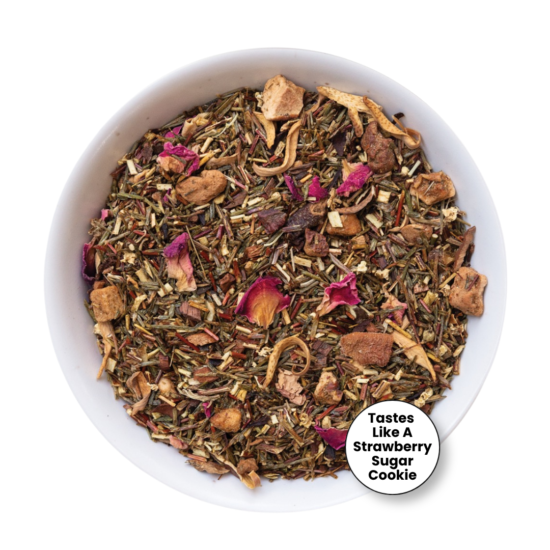 A top-down view of a white bowl filled with a loose-leaf herbal tea blend. The tea contains dried green herbs, brown pieces, and pink dried flower petals.