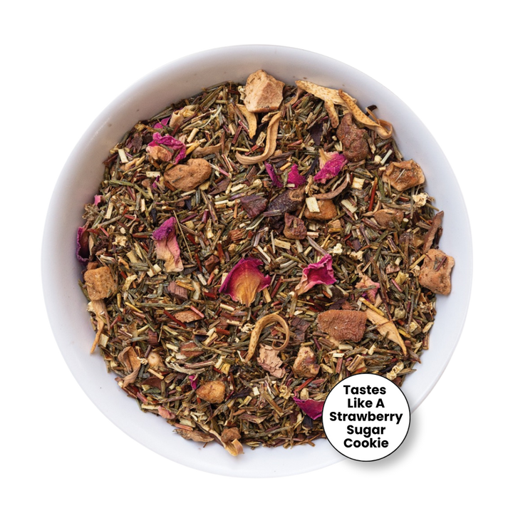 A top-down view of a white bowl filled with a loose-leaf herbal tea blend. The tea contains dried green herbs, brown pieces, and pink dried flower petals.