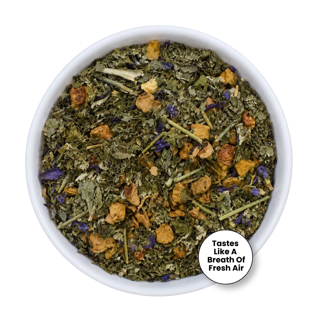 A top-down view of a white bowl filled with dried herbal tea blend, featuring green leaves, yellow-brown flower petals, and small purple accents, with a circular badge that reads &