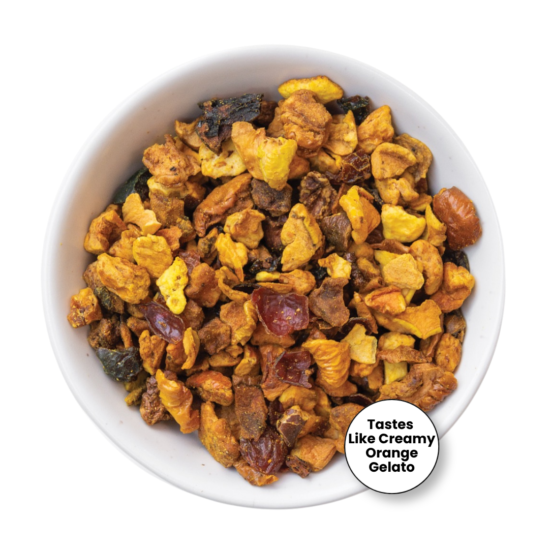 A top-down view of a white bowl filled with a colorful, chunky fruit gelato mix. The mixture contains pieces of yellow mango, orange, dark dates, and brown dates, creating a creamy, multicolored texture.