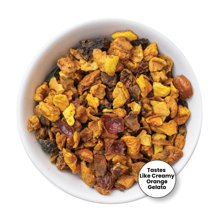 A top-down view of a white bowl filled with a colorful, chunky fruit gelato mix. The mixture contains pieces of yellow mango, orange, dark dates, and brown dates, creating a creamy, multicolored texture.