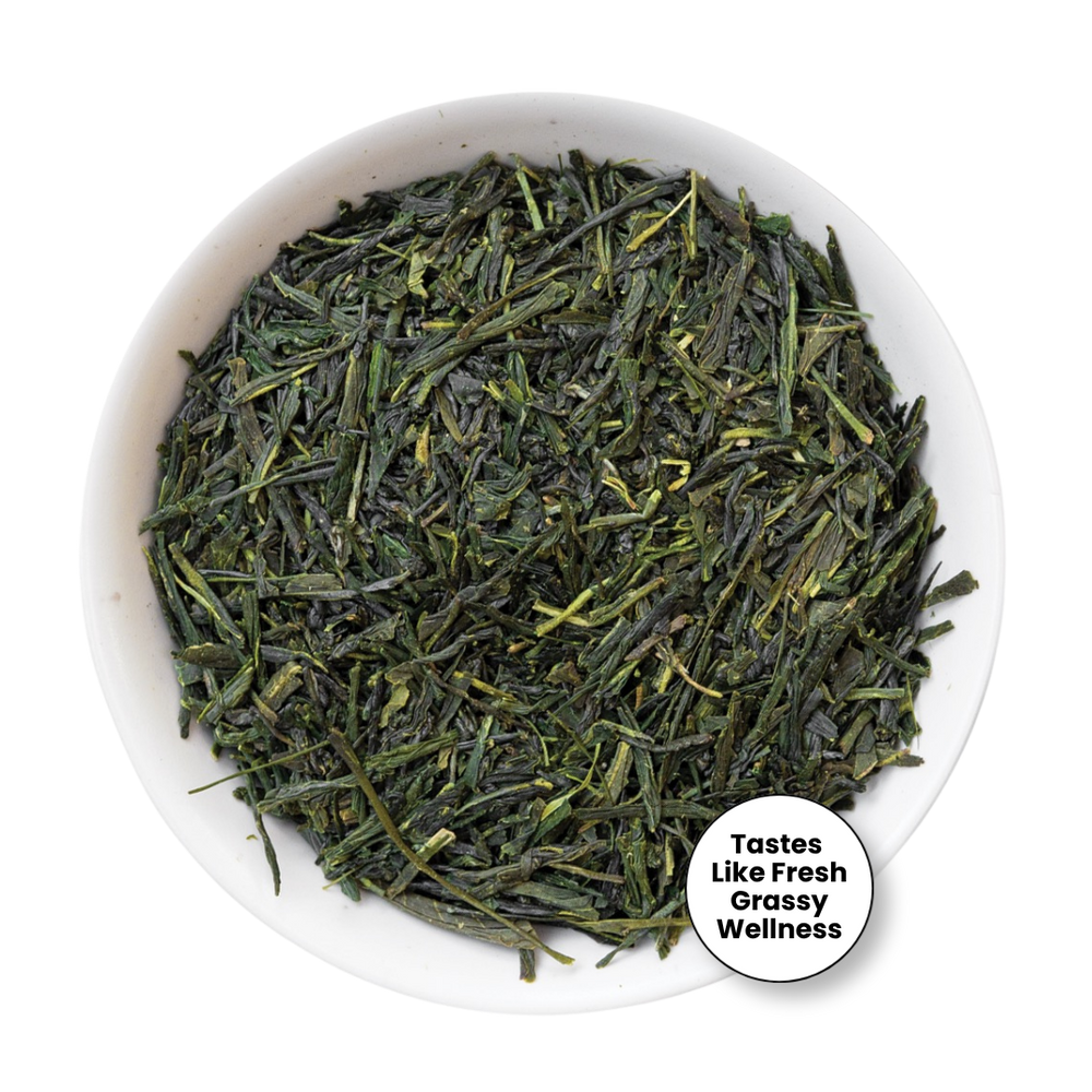 A top-down view of loose-leaf green tea leaves in a white bowl, with a small circular badge in the lower right that reads 'Tastes Like Fresh Grassy Wellness'.
