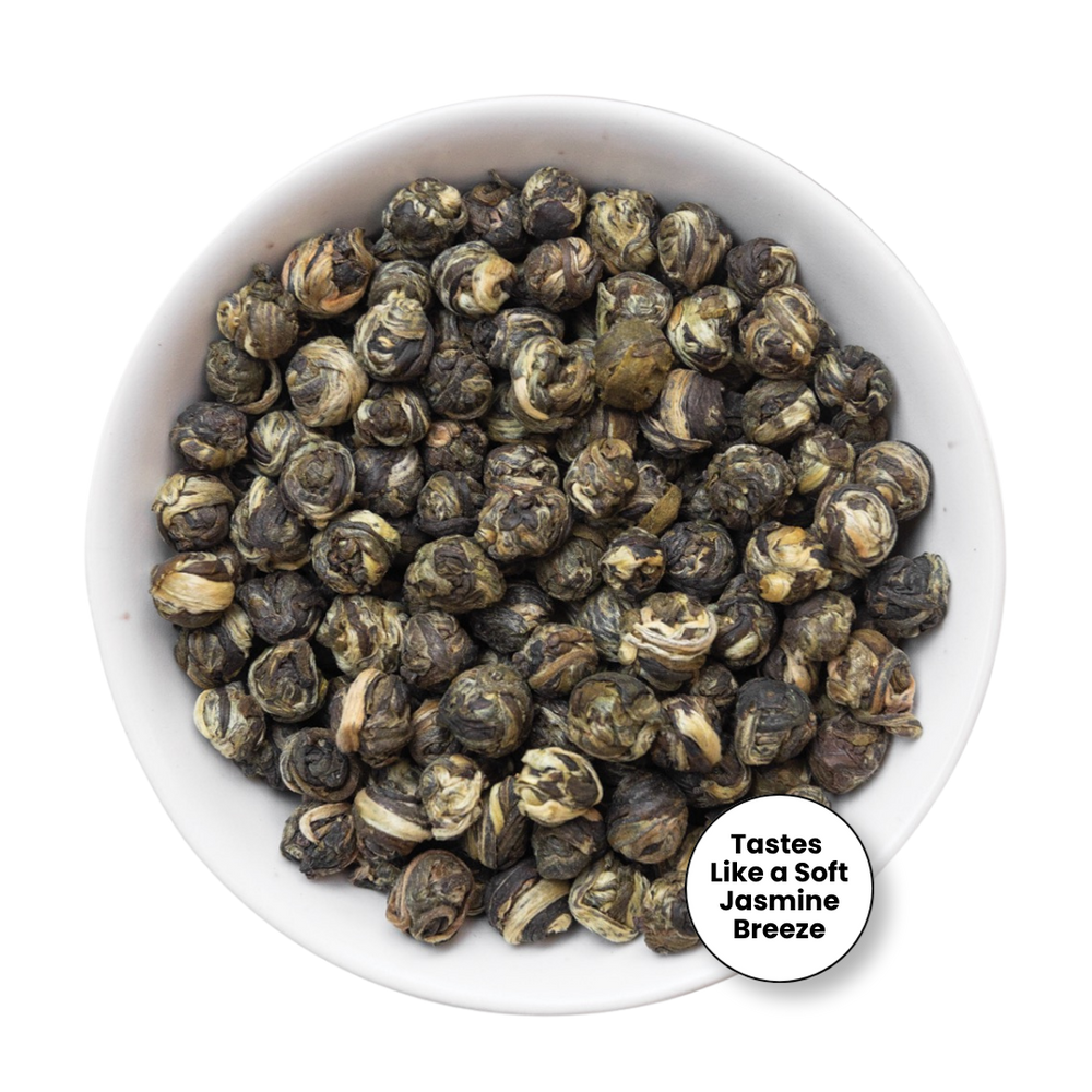 A top-down view of loose-leaf jasmine-breeze flavored tea leaves, which are rolled into small buds, displayed in a white ceramic bowl. A circular white sticker overlay in the bottom right corner reads 'Tastes Like a Soft Jasmine Breeze'.