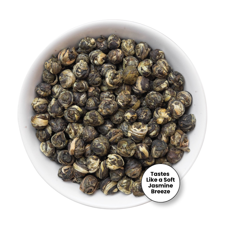 A top-down view of loose-leaf jasmine-breeze flavored tea leaves, which are rolled into small buds, displayed in a white ceramic bowl. A circular white sticker overlay in the bottom right corner reads &