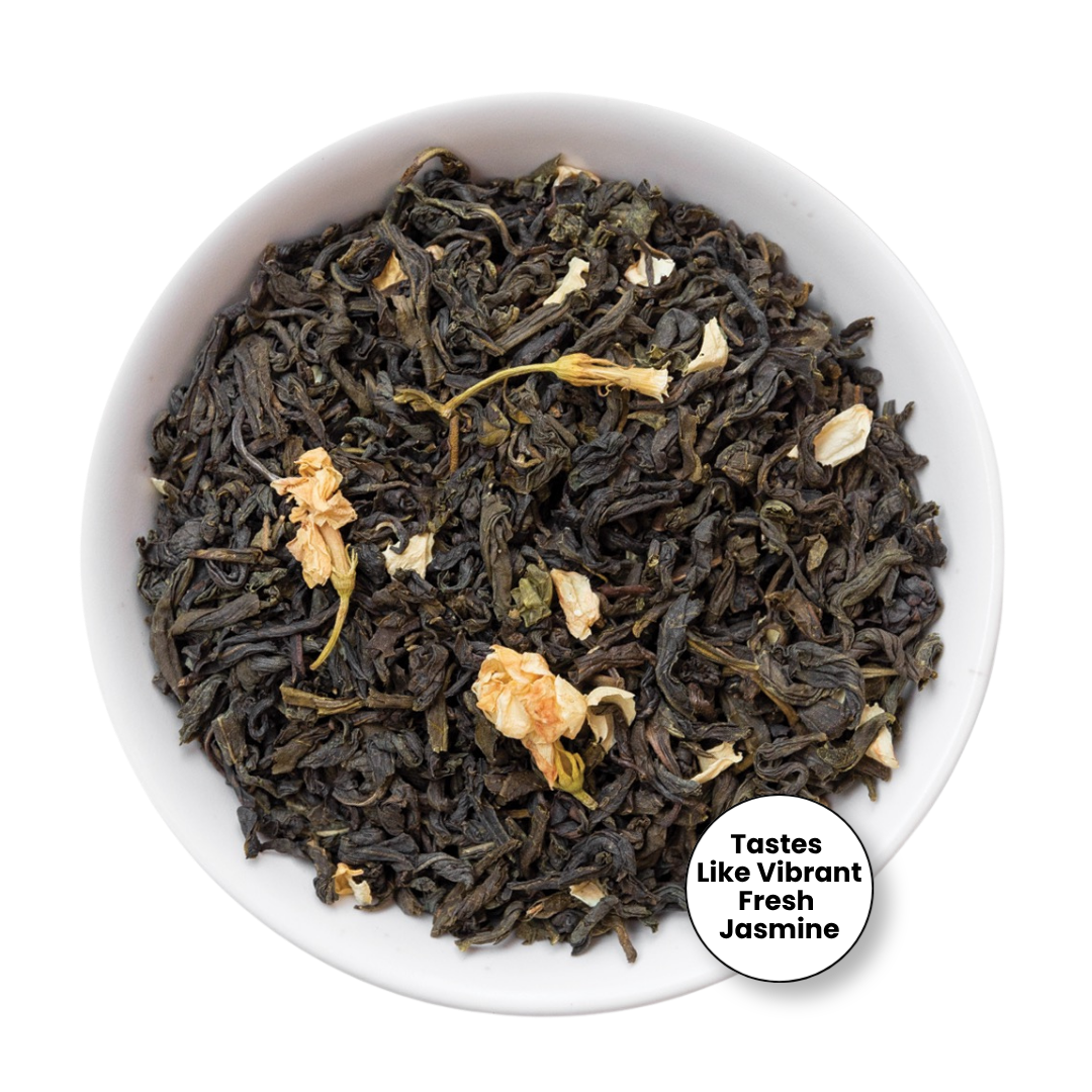 A top-down view of loose-leaf jasmine tea in a white bowl, featuring dark green tea leaves mixed with dried pale yellow jasmine blossoms. A circular badge in the bottom right corner reads &