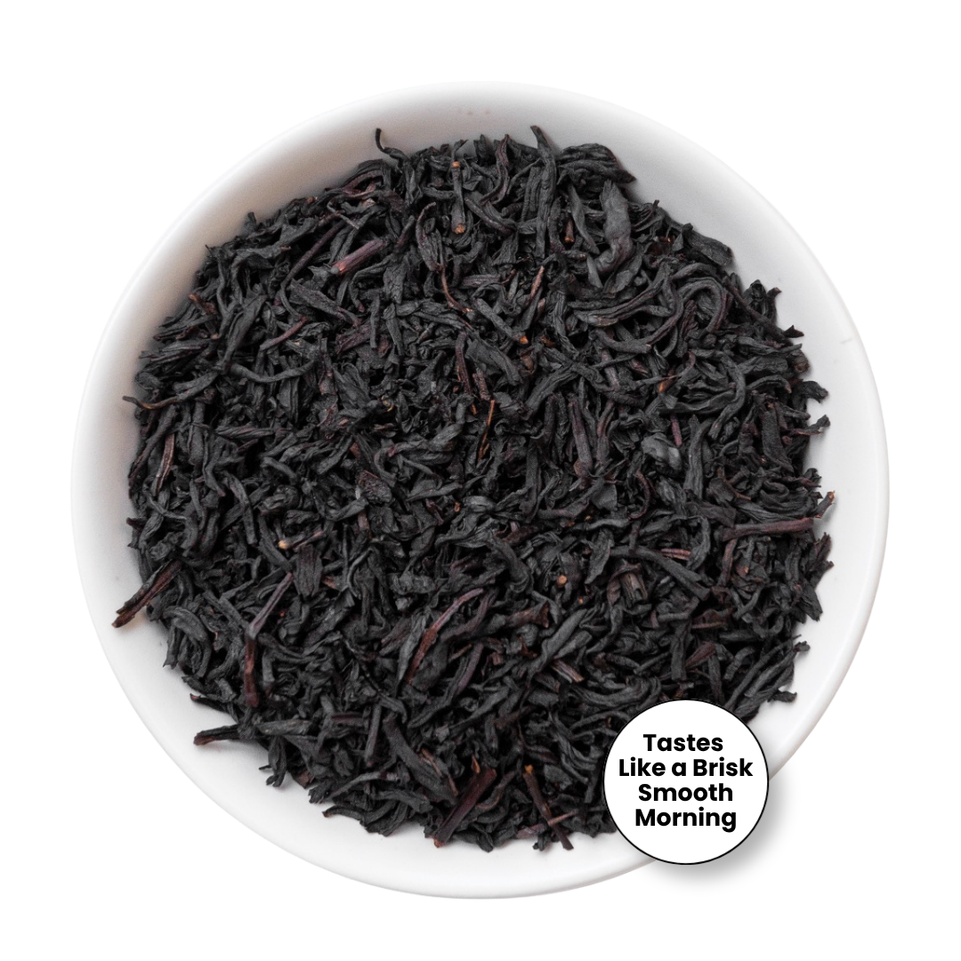 Dark black tea leaves piled in a white bowl, with a small circular badge in the lower right that reads &