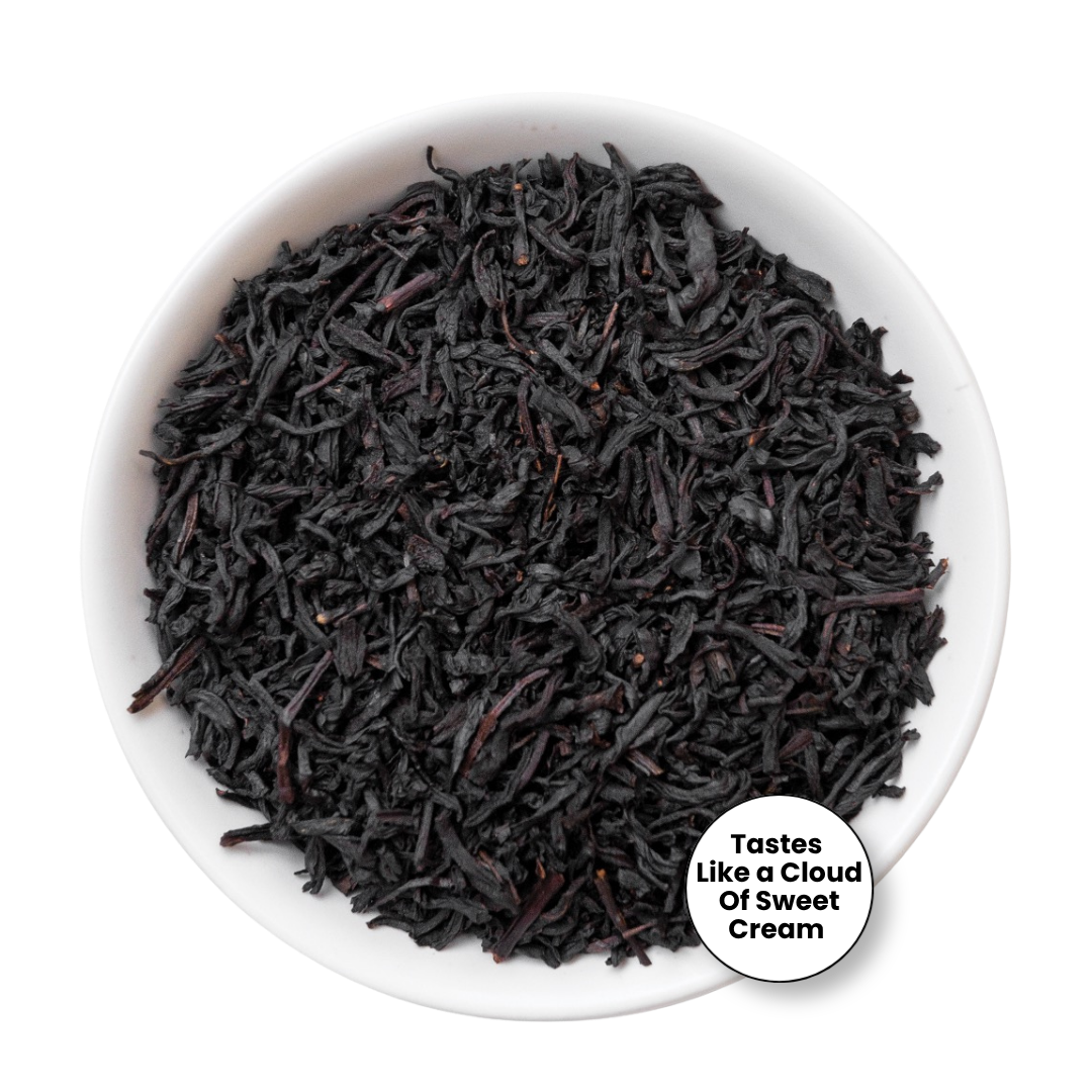A top-down view of dark, curly tea leaves in a white bowl, with a white circular badge in the lower right that reads &