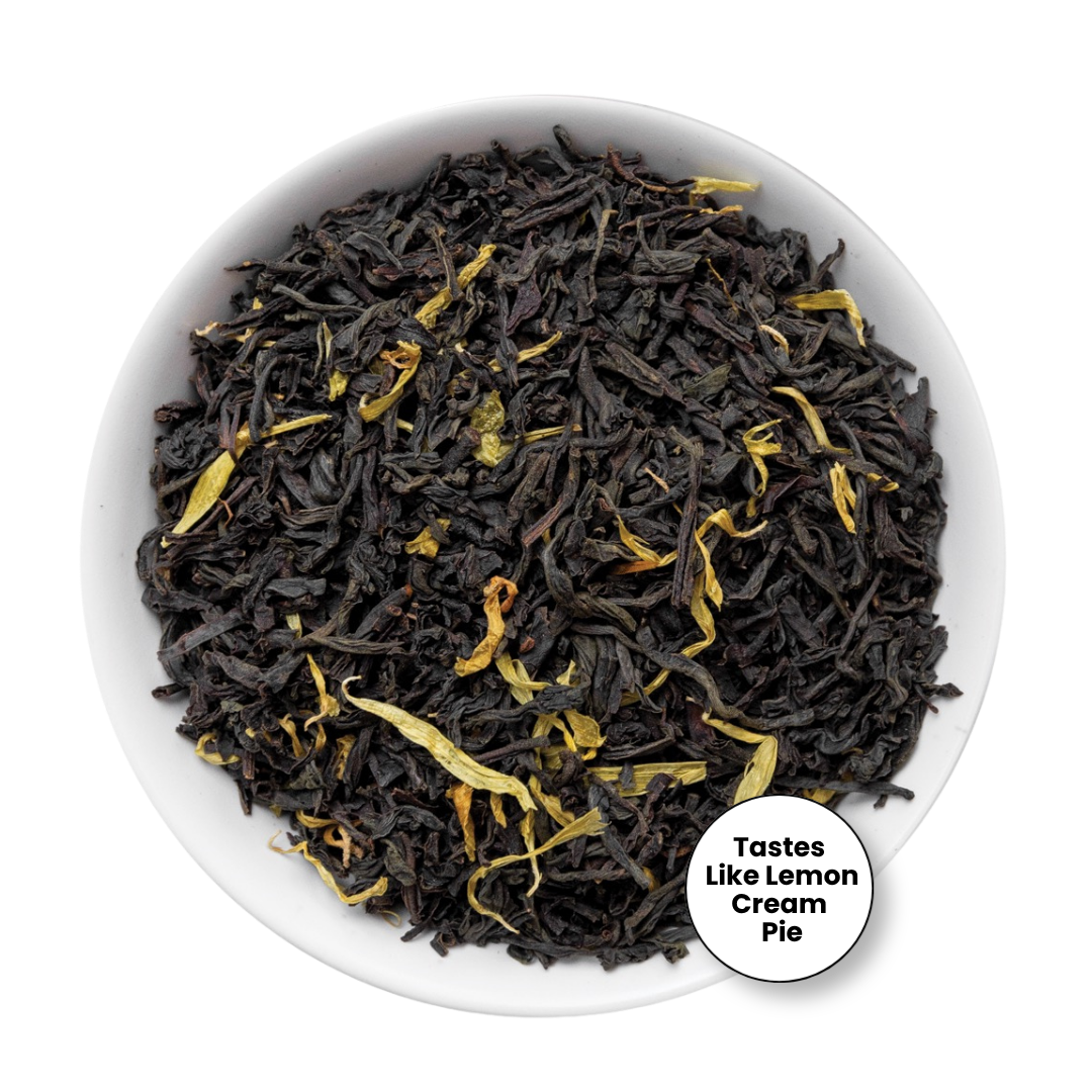 A top-down view of loose-leaf tea in a white bowl, featuring dark brown to black tea leaves with scattered dried yellow lemon peel pieces. A circular badge in the lower right corner reads &