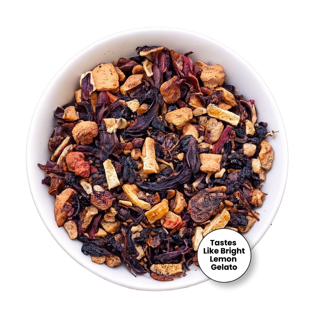 A top-down view of a white bowl filled with dried herbal tea blend, featuring dark purple hibiscus flowers, light tan citrus pieces, and small red fruit pieces. A circular badge in the lower right reads 'Tastes Like Bright Lemon Gelato'.