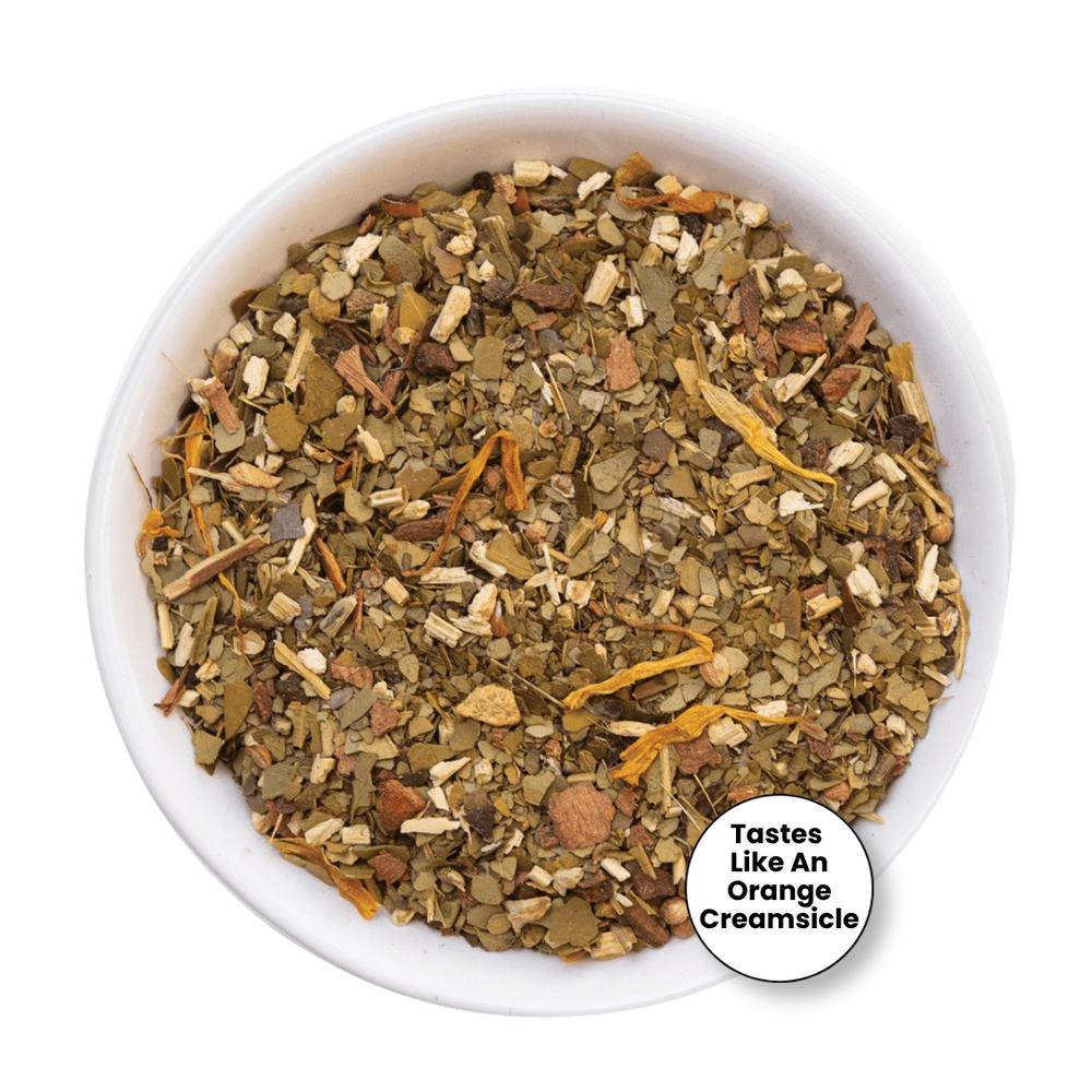 A top-down view of a loose-leaf herbal tea blend in a white bowl, with a small circular badge in the lower right that reads 'Tastes Like An Orange Creamsicle'. The tea contains dried green leaves, light tan pieces, and orange-yellow citrus slices on a white background.