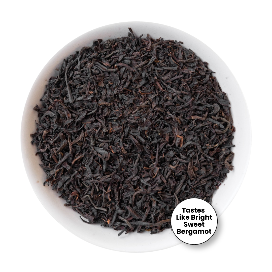 A top-down view of loose-leaf tea in a white bowl, with a small circular badge in the lower right that reads &