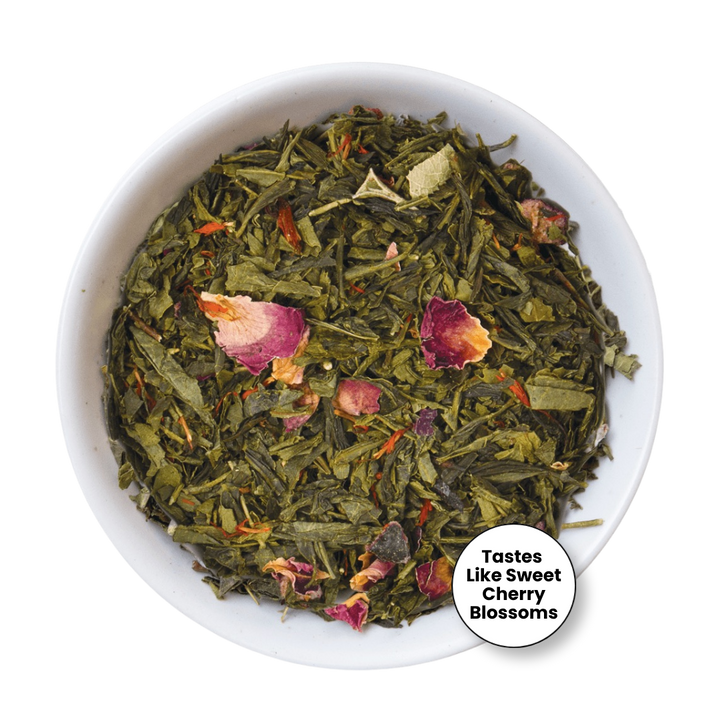 A top-down view of loose-leaf herbal tea in a white bowl, featuring green tea leaves mixed with dried pink and red flower petals. A circular badge in the bottom right corner reads &