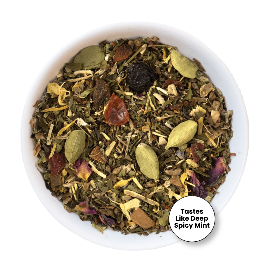A top-down view of a white bowl filled with a loose herbal tea blend. The tea contains green cardamom pods, dried flowers, and small brown pieces.