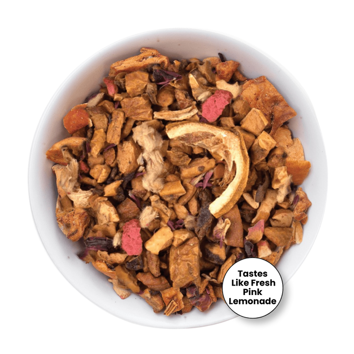 A top-down view of a white bowl filled with dried fruit and vegetable pieces for pet chews, including orange slices, pink dried pieces, and brown root vegetables. A circular badge in the bottom right corner reads &