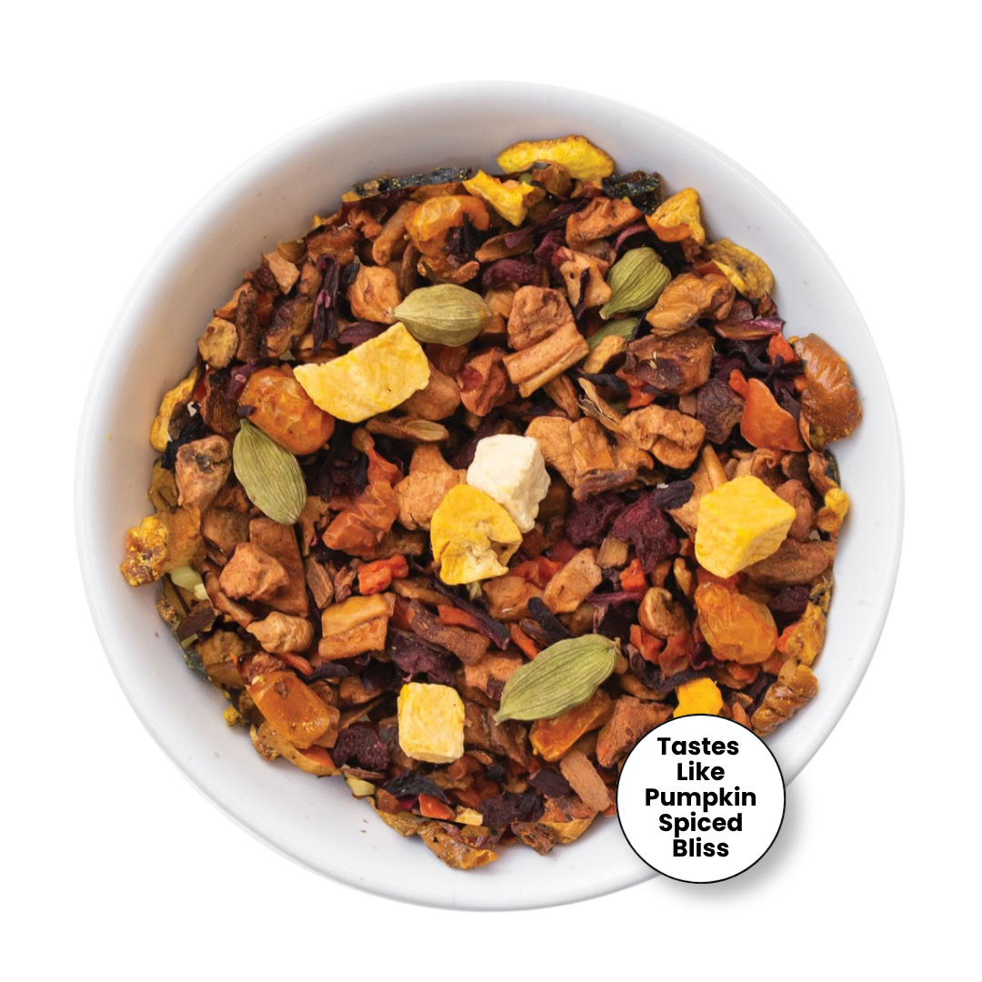 A top-down view of a white bowl filled with a colorful herbal tea blend containing dried fruits, spices, and green cardamom pods, with a circular label that reads &