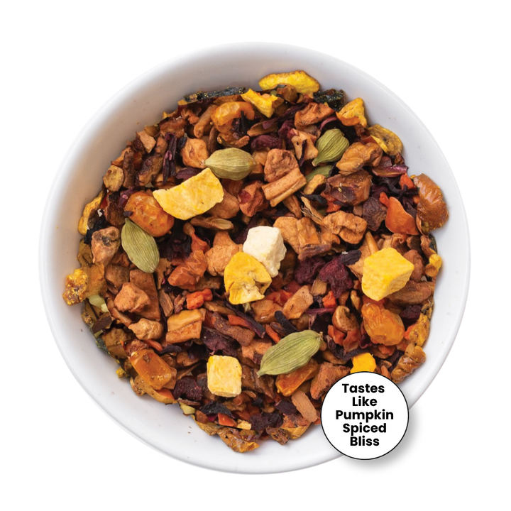 A top-down view of a white bowl filled with a colorful herbal tea blend containing dried fruits, spices, and green cardamom pods, with a circular label that reads &