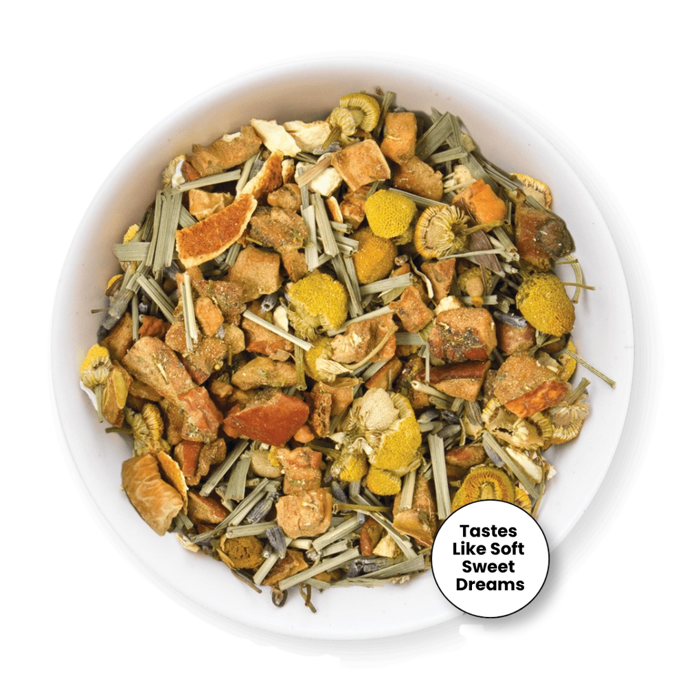 A top-down view of a white bowl filled with a loose herbal tea blend. The tea contains dried orange slices, yellow flower petals, green stems, and brown roots.