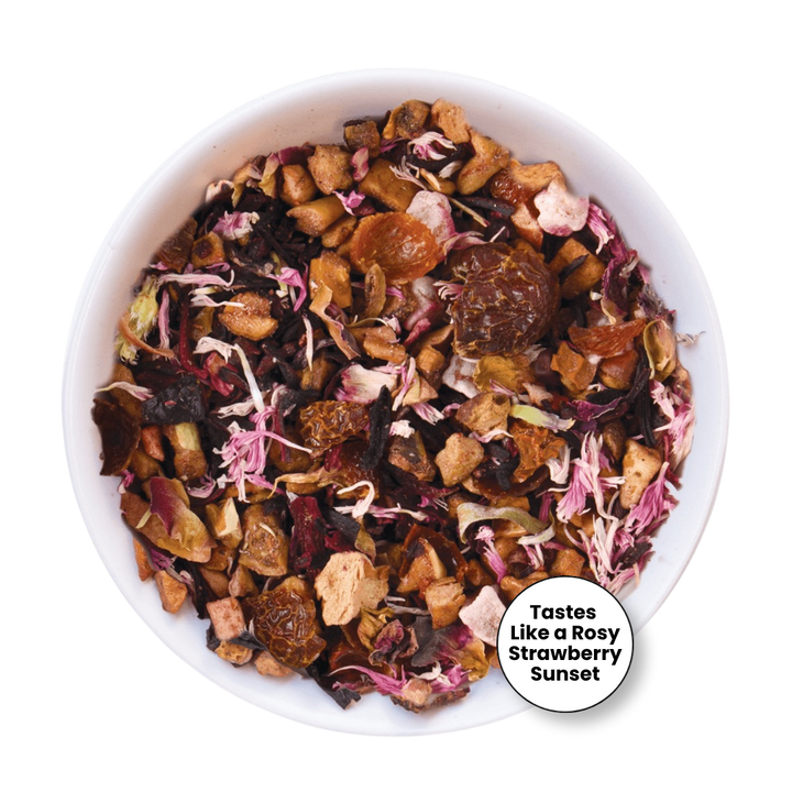 A top-down view of a white bowl filled with loose-leaf herbal tea blend, featuring dried flowers, fruit pieces, and tea leaves. A circular badge in the lower right reads &