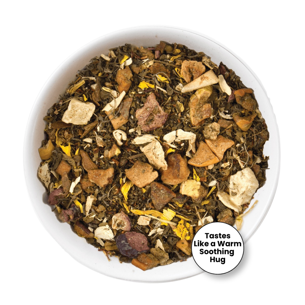 A top-down view of a white bowl filled with a loose herbal tea blend. The tea contains dark green leaves, light brown pieces, pale beige chunks, and small yellow accents.