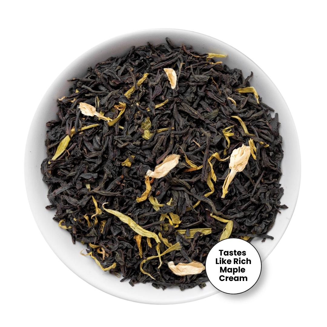A top-down view of a white bowl filled with dark black tea leaves mixed with dried pale yellow flower petals, with a circular badge in the lower right that reads &
