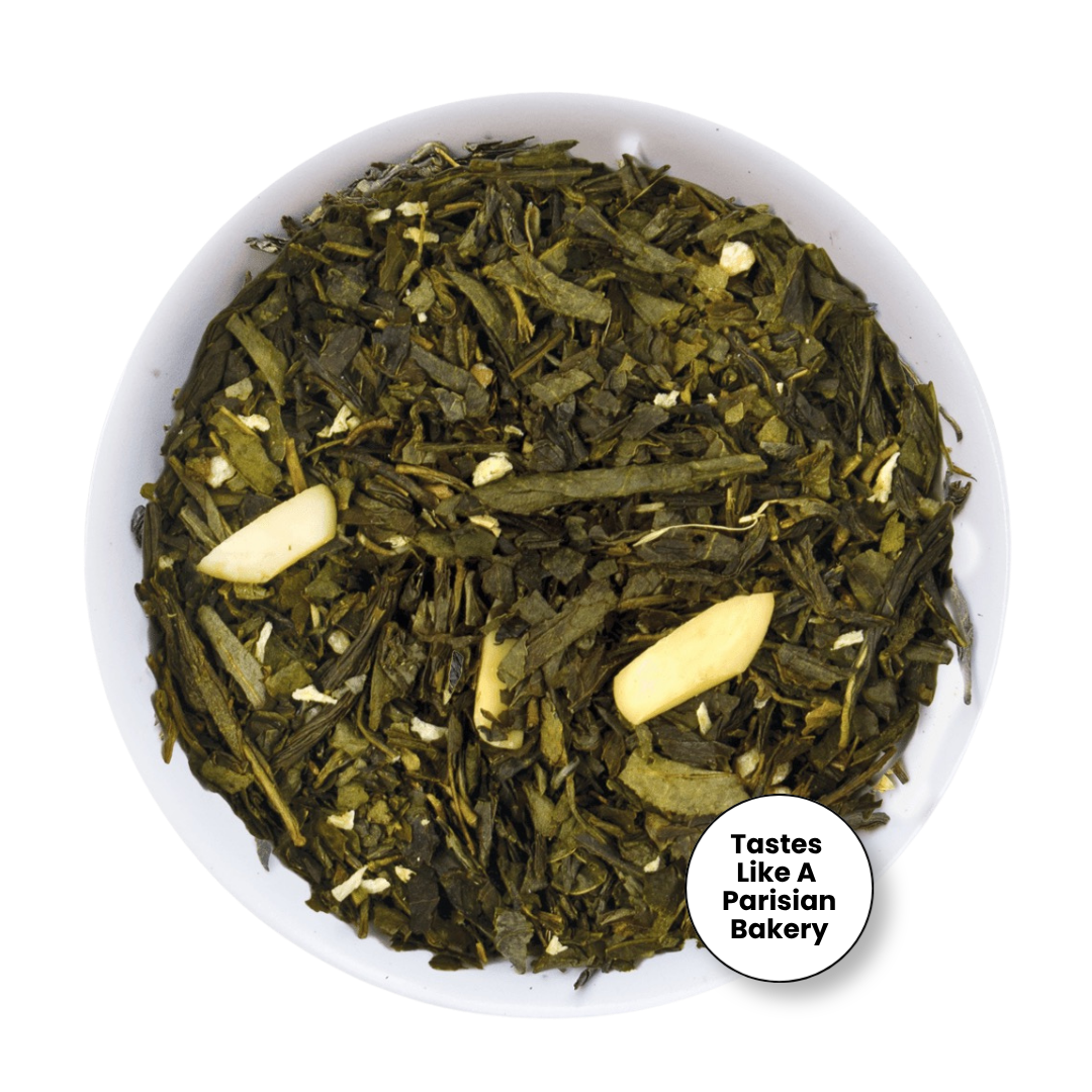 Loose leaf tea in a white bowl, featuring dark green tea leaves with two pale garlic cloves and small white flower petals. A white circular badge in the bottom right corner reads &