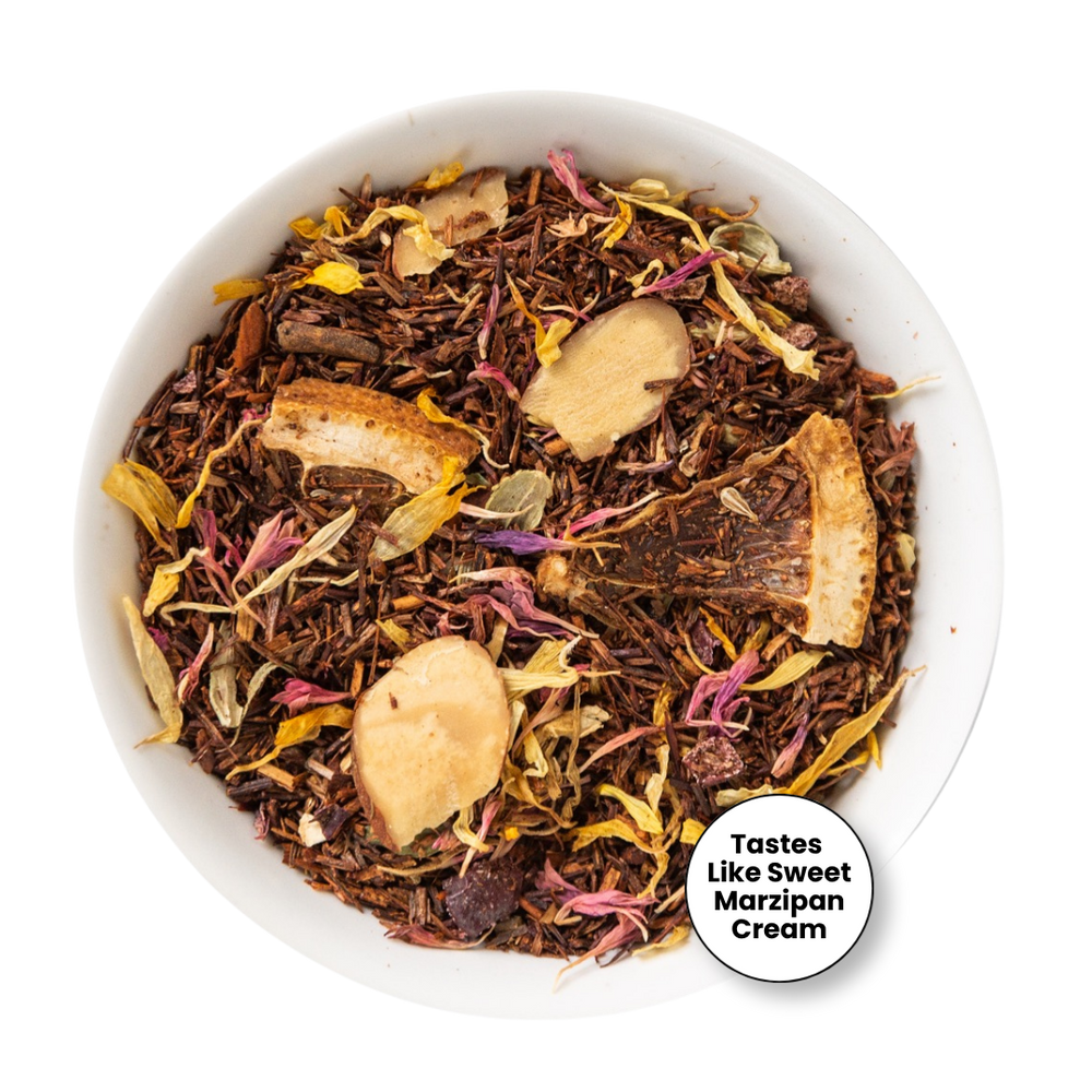 A top-down view of loose-leaf herbal tea in a white bowl, featuring dark brown tea leaves mixed with dried flowers in pink, yellow, and purple, and several light tan dried fruit slices. A white circular badge in the bottom right corner reads 'Tastes Like Sweet Marzipan Cream'.