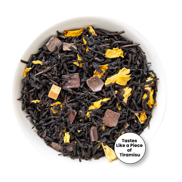 A top-down view of loose-leaf tea in a white bowl, featuring dark brown tea leaves with pieces of dark chocolate and bright yellow dried flower petals. A circular badge in the bottom right corner reads &