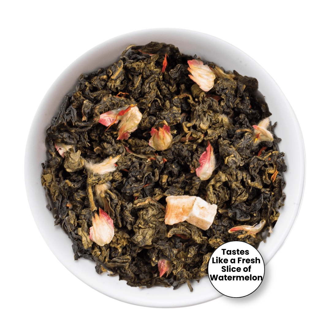 A top-down view of loose-leaf tea in a white bowl, featuring dark green tea leaves mixed with pale pink watermelon blossom pieces. A circular badge in the bottom right corner reads, &