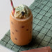 Milkshake with ice cream and a straw on a checkered cloth, next to a Tealish Chocolate Mint tea package.