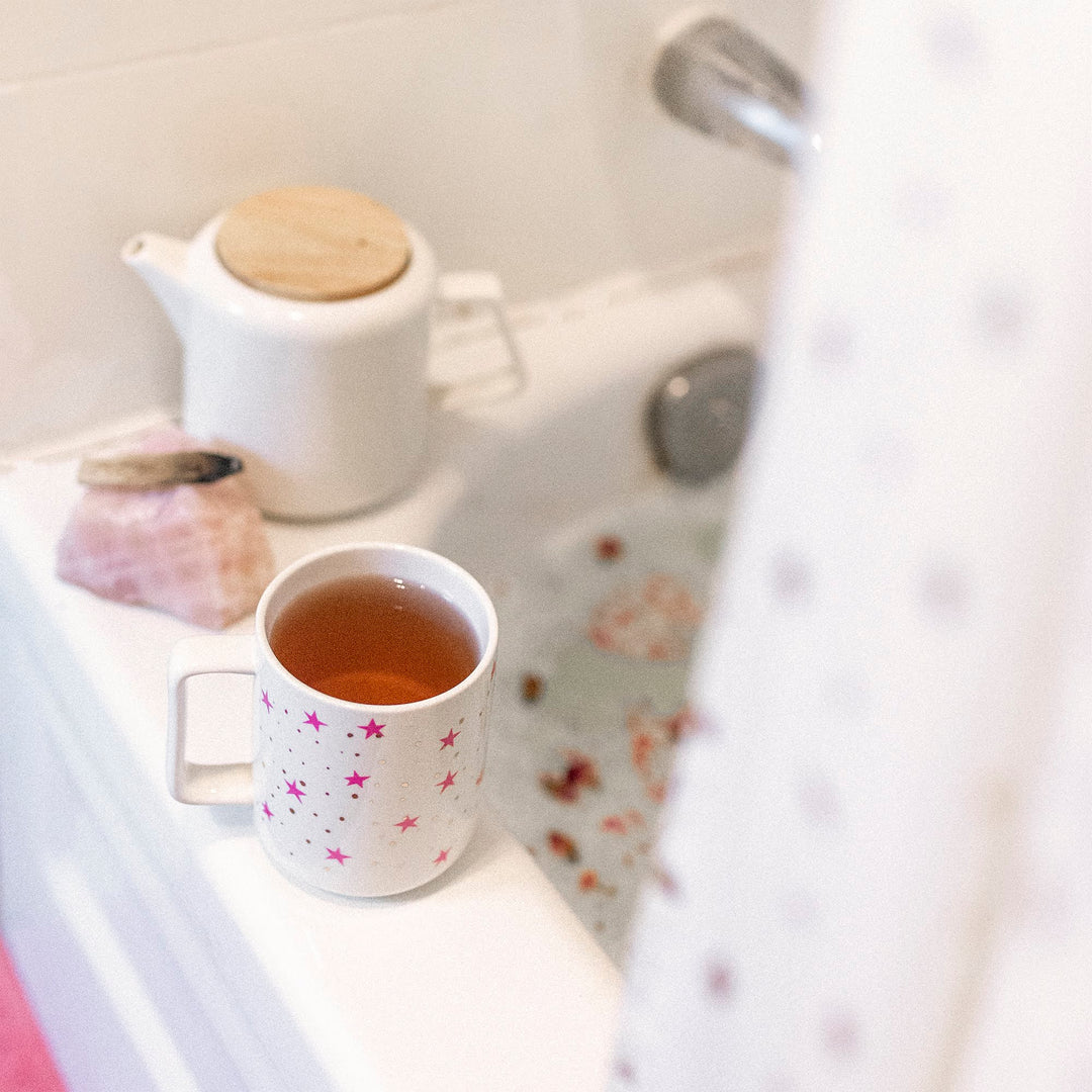 A cup of tea with bergamot flavor, commonly associated with earl grey, is placed on a windowsill with a view of a white teapot and a floral-patterned mug.