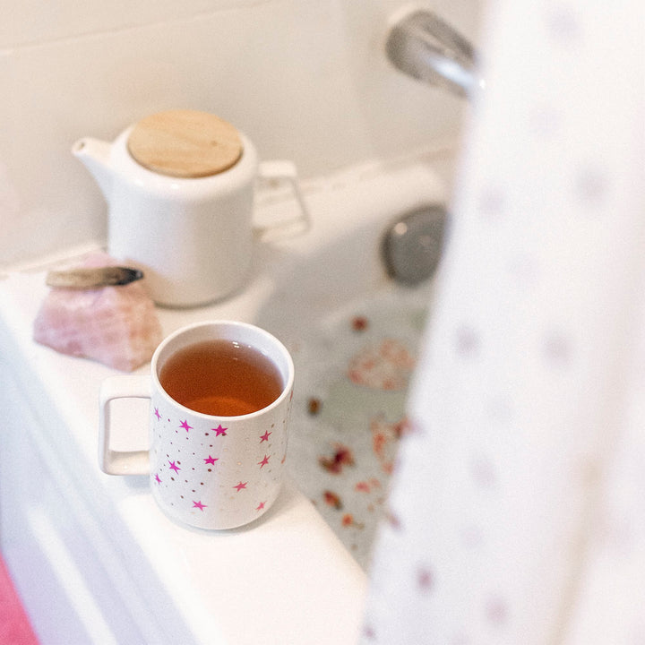 A cup of tea with bergamot flavor, commonly associated with earl grey, is placed on a windowsill with a view of a white teapot and a floral-patterned mug.