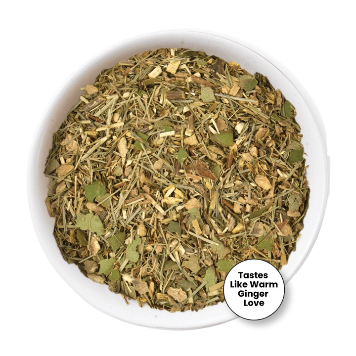 A top-down view of a white bowl filled with a loose herbal tea blend. The blend contains dried green leaves, light brown roots, and stems.