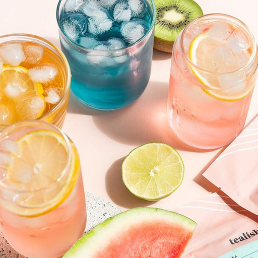 Assorted iced teas displayed with corresponding loose leaf tea packages, accompanied by fruits and citrus slices.